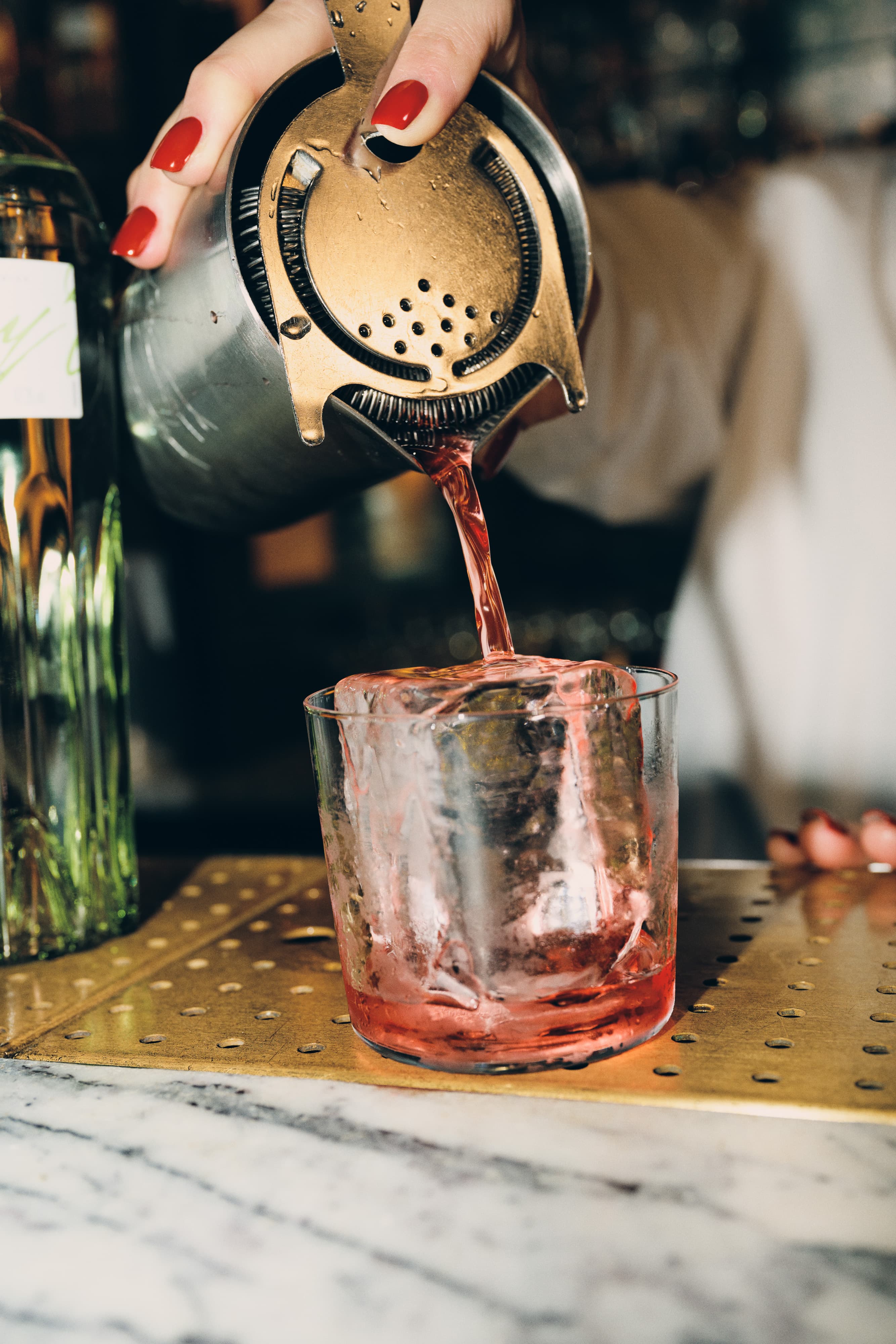 A hand straining a cocktail into a glass with on large ice cube