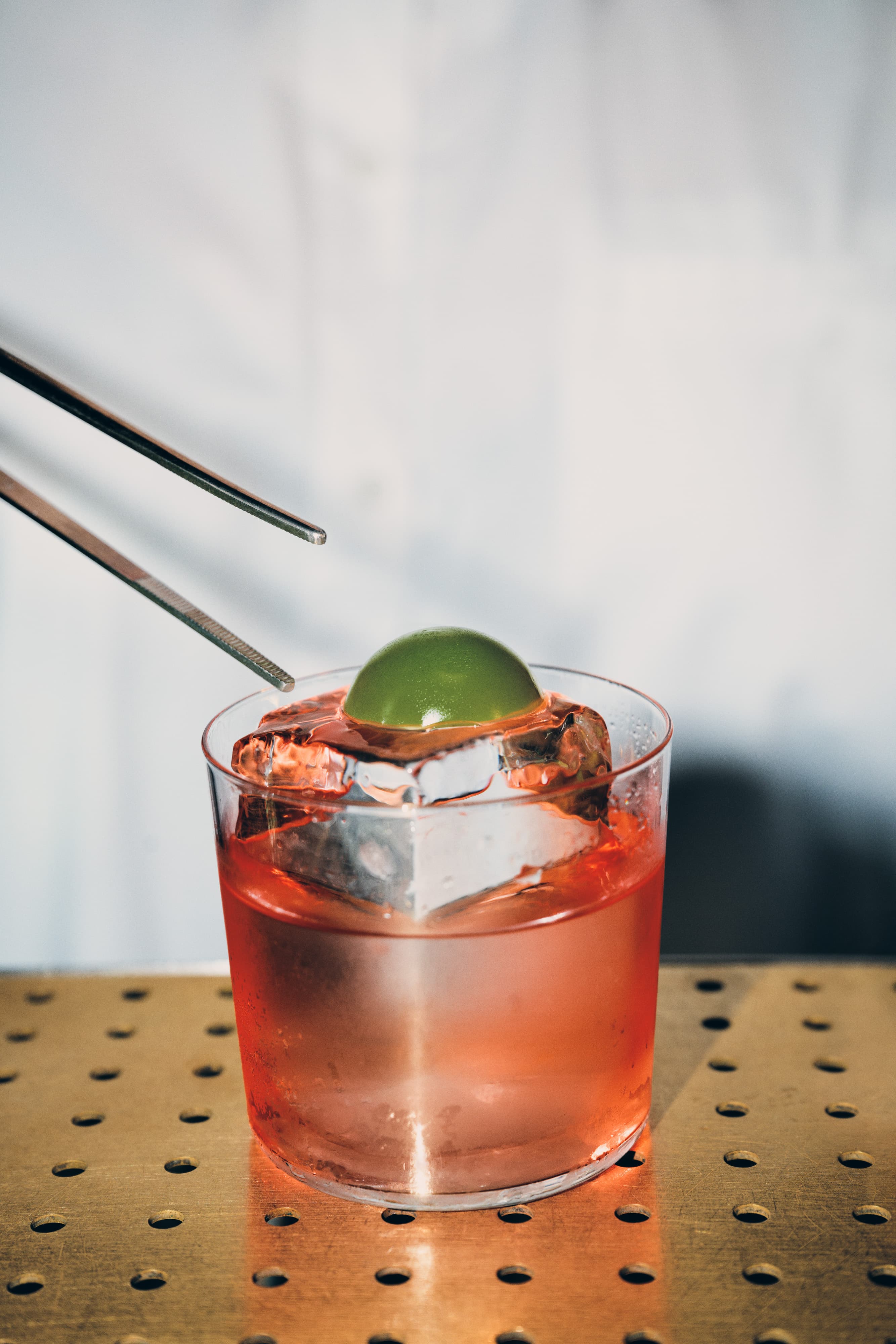 Tongs placing a tarragon on top of a large ice cub in a cocktail.