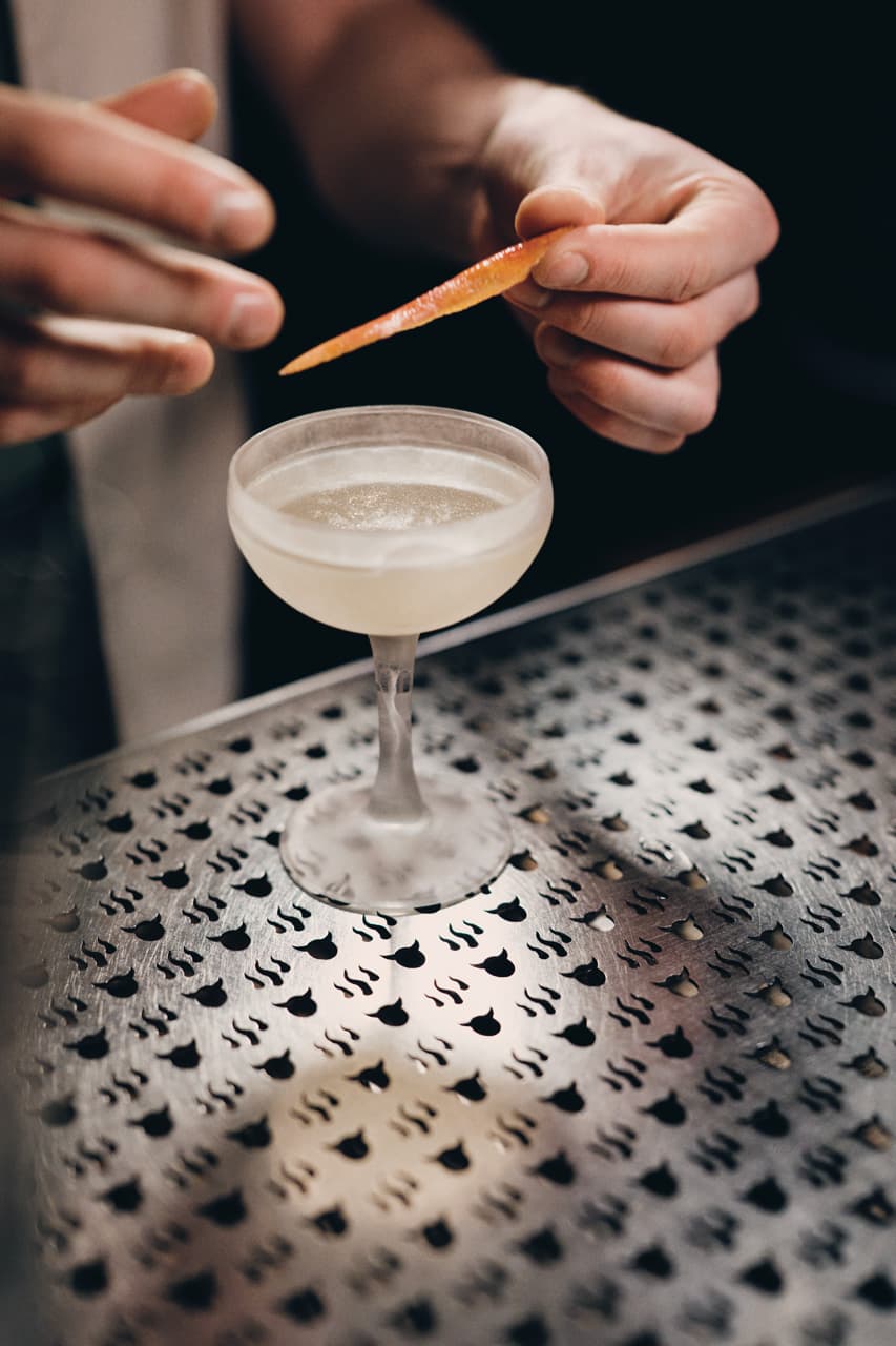 Two hands garnishing a cocktail with a blood orange peel.