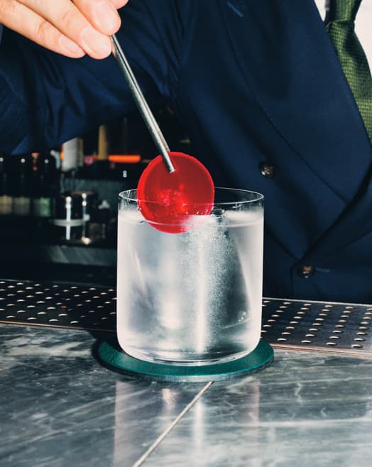 A person placing a sun dried tomato/mirto distillate garnish into a Gin Rickey cocktail