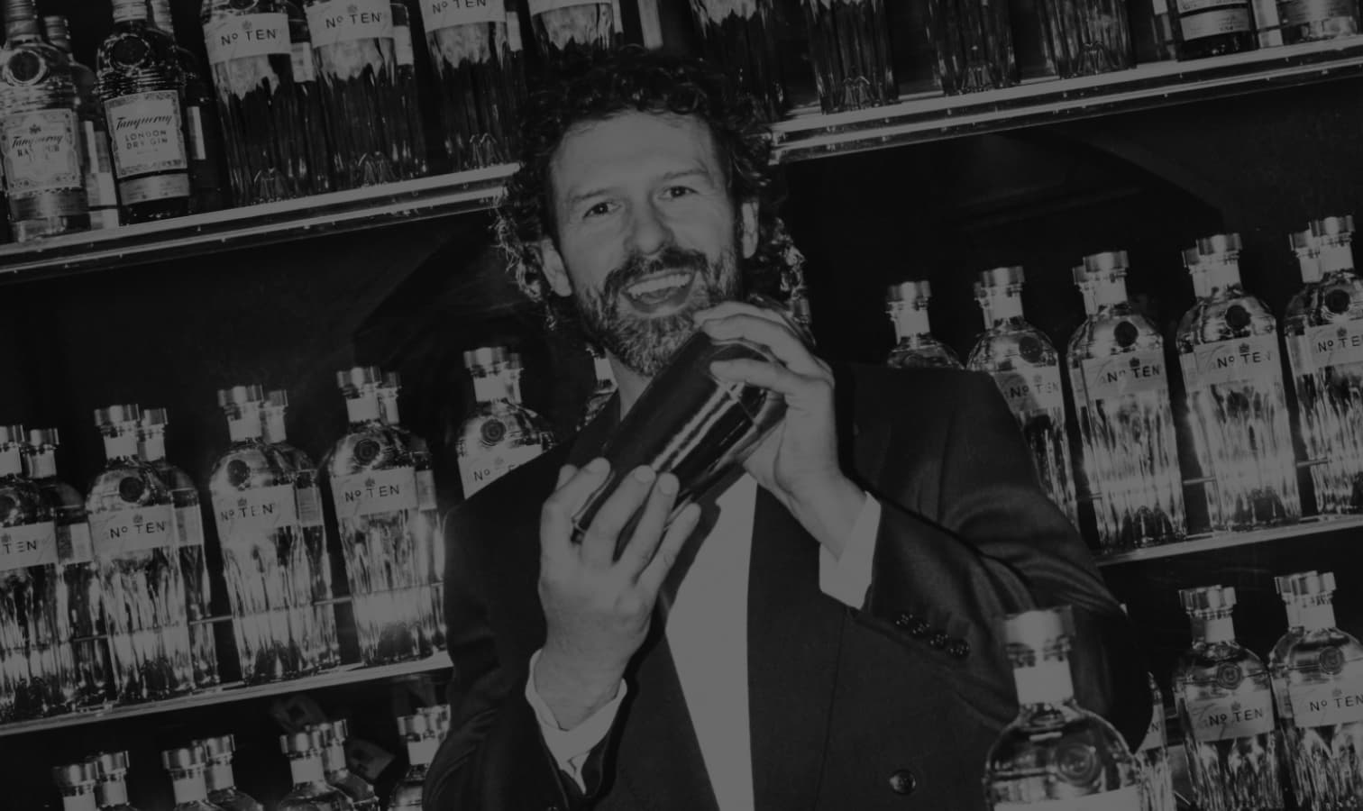 Matteo Di ienno holding a cocktail shaker in front of a wall of Tanqueray No. Ten bottles.