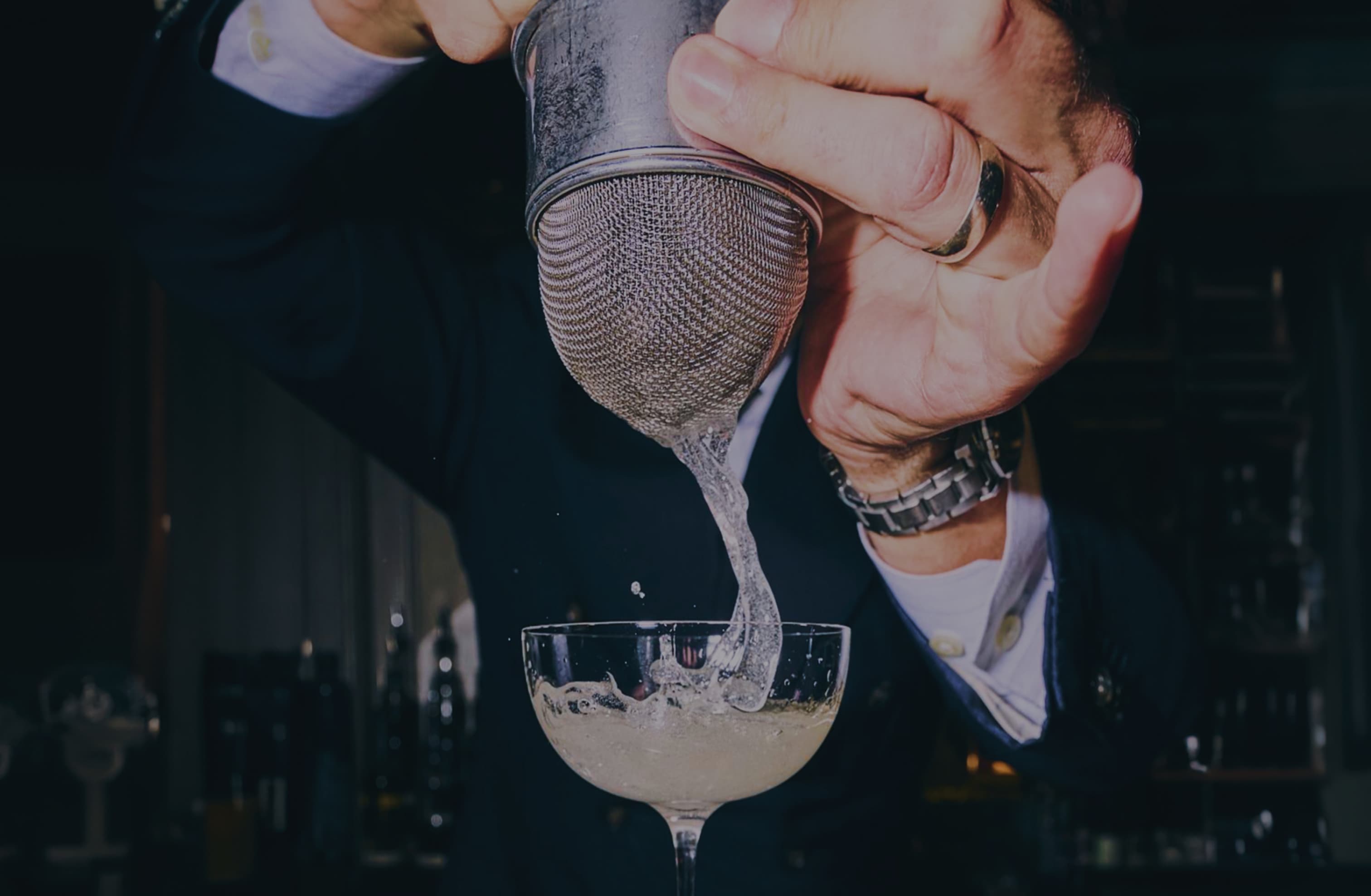 A hand straining a cocktail into a glass